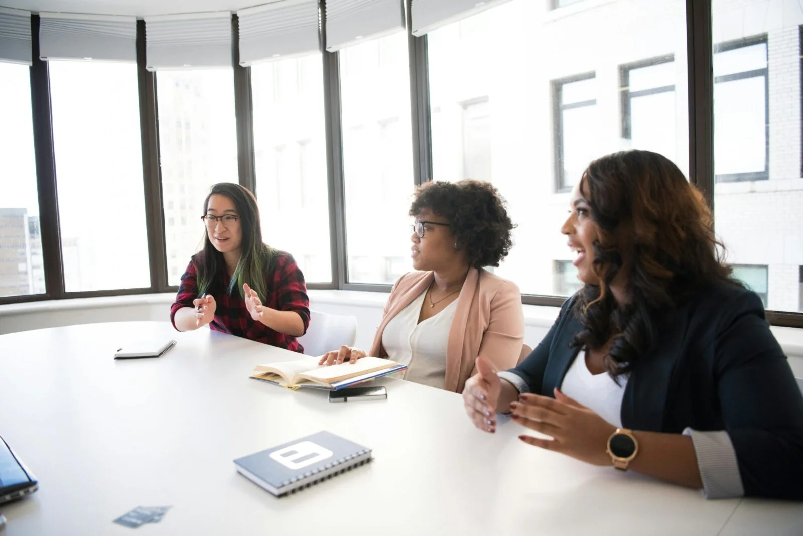 Crop unrecognizable coworkers in formal wear standing at table with laptop and documents while greeting each other before meeting